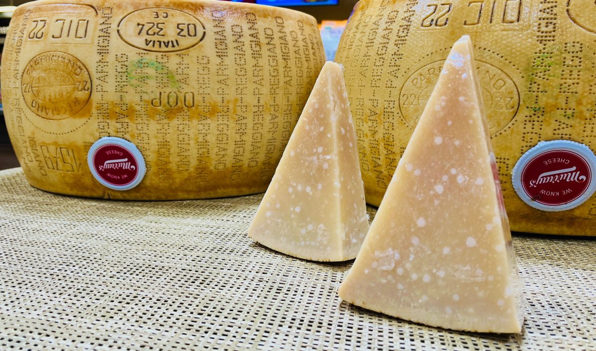 Two slices of Parmigiano reggiano along with two wheels. The white specks aren't mold but tyrosine crystals which are edible and contribute to the flavor of the cheese.